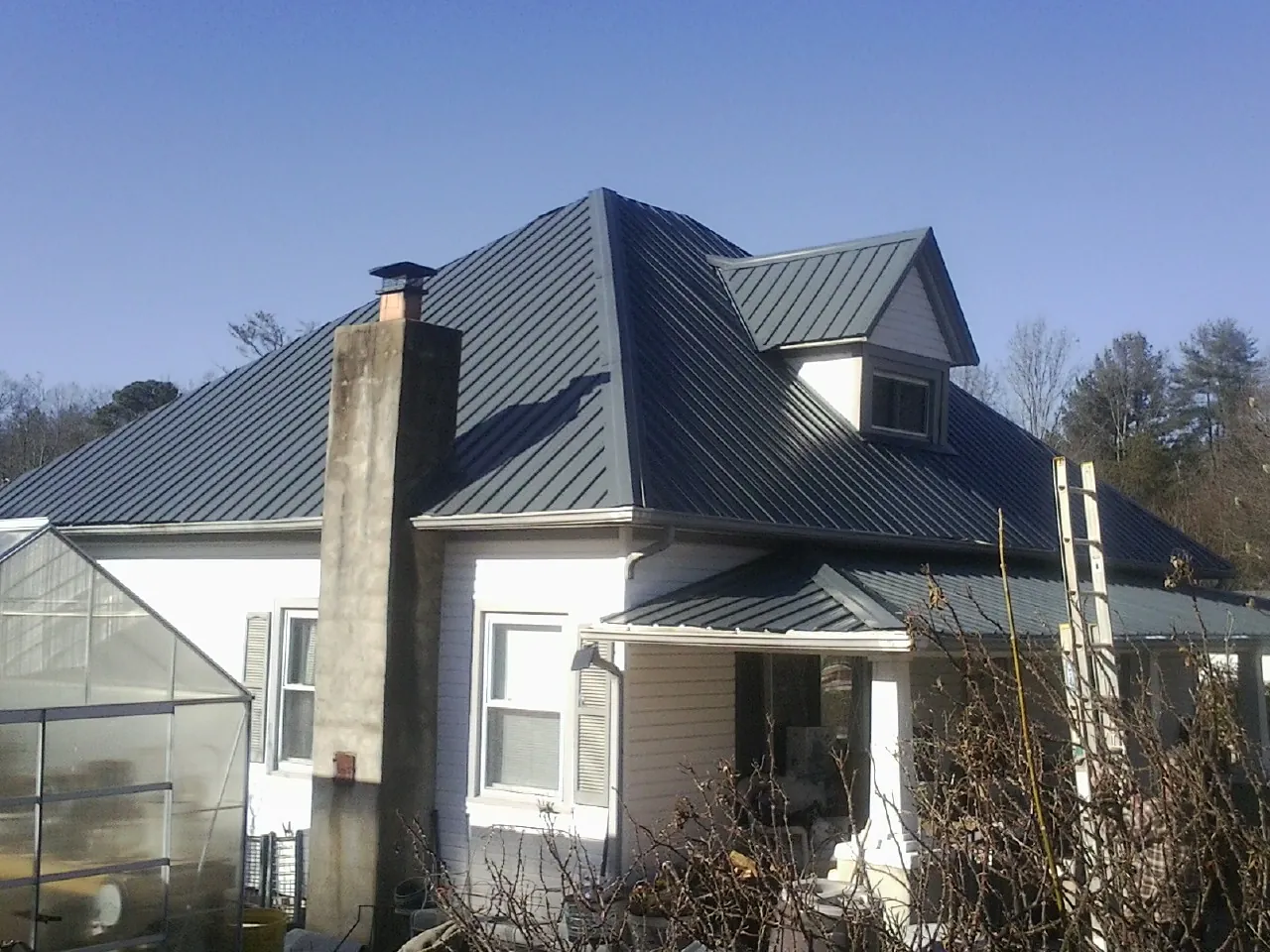 Dark blue standing seam metal roof on a white farmhouse with dormer — Slate & Tile Roof Repair by Roofing Brothers in Boerne