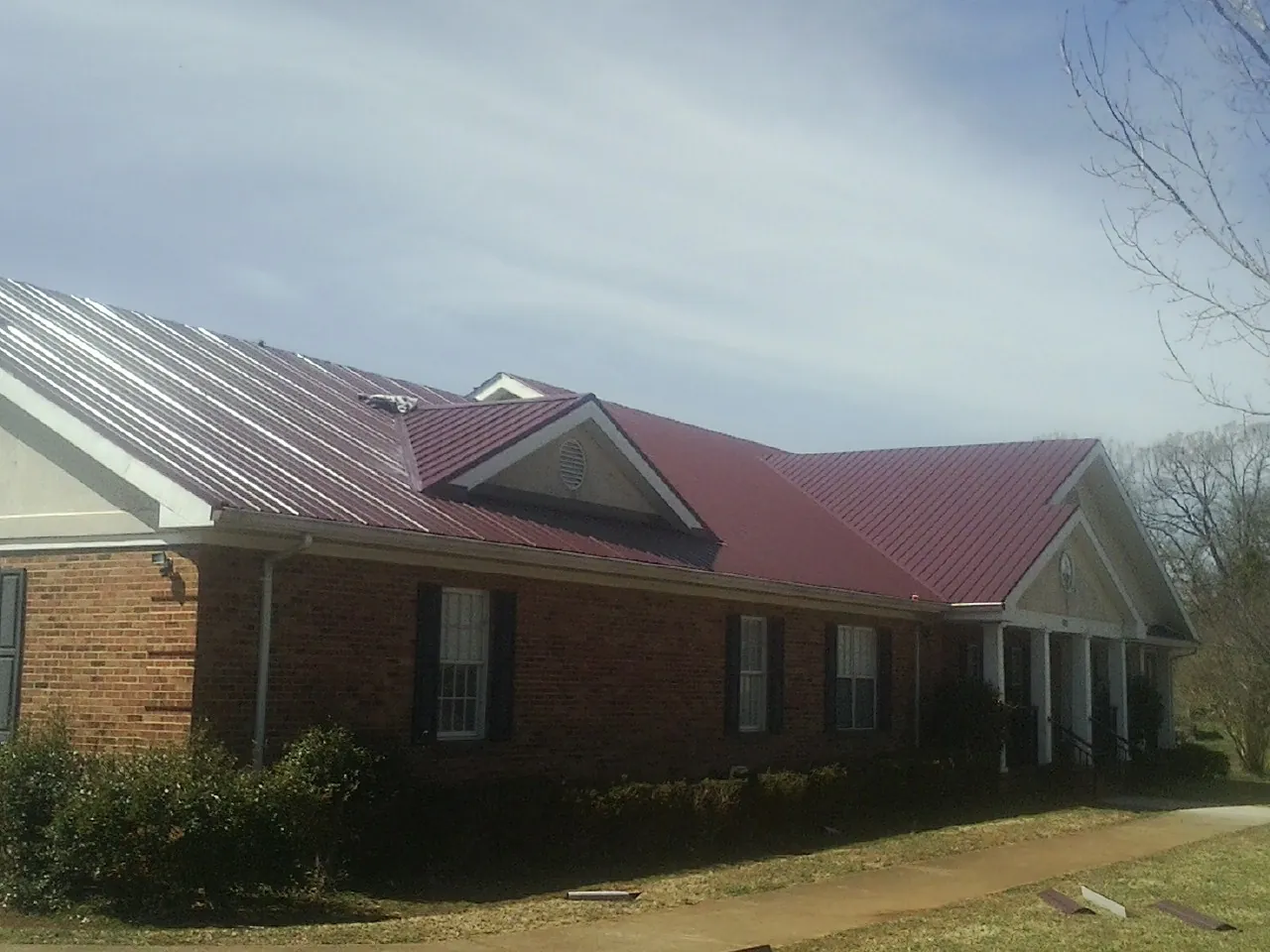 Red metal roof with gabled entries on a long brick building, from a Hail Damage Roof Repair job in Boerne