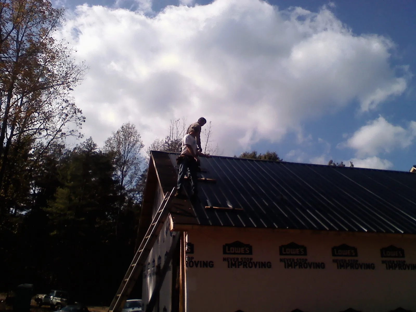 Roofer fastening dark metal panels high against a cloudy sky, from a Roof Inspection job in Boerne