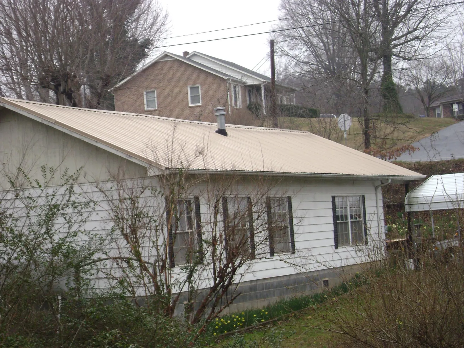 Tan metal roof on a white sided house set into a hillside — Commercial Roofing by Roofing Brothers in Boerne